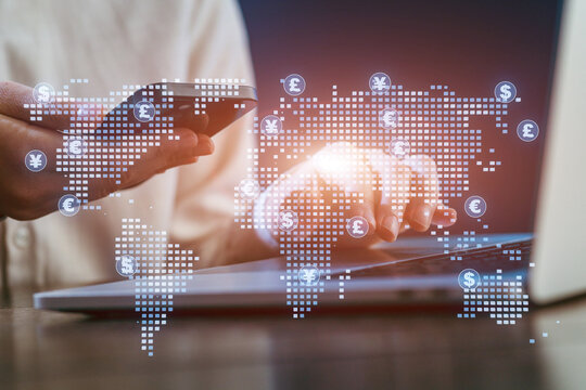 Person using smartphone and laptop with world map overlay displaying currency symbols in a modern workspace