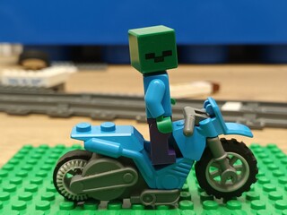 Fototapeta premium A LEGO Minecraft zombie character figure riding a blue LEGO motorcycle, placed on a green baseplate
