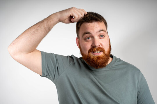 Red-haired bearded man looking confused and thoughtful on isolated background.