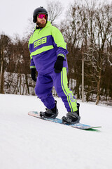 Bearded man snowboards down a snowy slope in vibrant winter gear