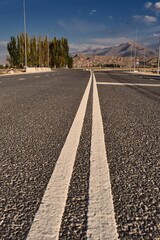 Fototapeta premium Road to the mountains of Kyrgyzstan. Asphalt highway with double solid lines leading towards the majestic Tian Shan mountain range. Travel and freedom.
