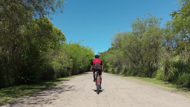 Male cyclist training outdoor. Aerial view, drone following, tracking shot. Cyclist riding a Mountain Bike MTB through a city natural reserve / park. Gravel biking concept. Cyclist red cycling jersey.