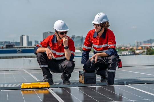 Solar engineer teamwork on rooftop maintenance boosts clean energy output under bright sky as two male technicians in safety gear inspect panel array with tools, focused and professional - Powered by Adobe
