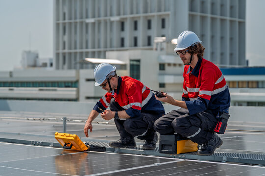 Solar engineer teamwork maintenance energy inspection rooftop panel bright daylight, two male technicians with hard hat and tool case coordinate repair and testing for reliable power supply