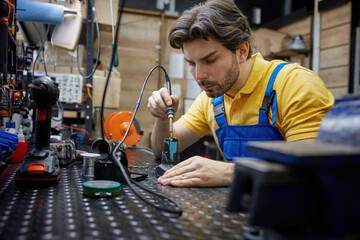 Skilled man worker is working on soldering iron in a workshop