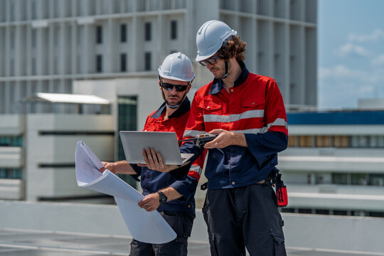 Engineer teamwork maintenance energy solar site planning rooftop, two male technician hard hat review plan and laptop with focus and care while inspection and repair ensure safety and power