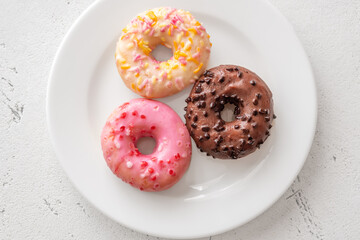 Pink white and chocolate glazed donuts arranged neatly on clean minimalist white plate