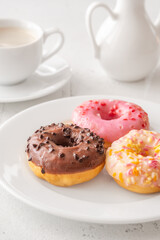 Trio of glazed donuts with coffee cup and pitcher in bright morning light