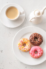 Trio of glazed donuts with coffee cup and pitcher in bright morning light