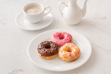 Trio of glazed donuts with coffee cup and pitcher in bright morning light