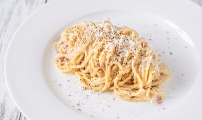 Creamy traditional carbonara served with grated parmesan on smooth white ceramic plate