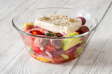 Fresh traditional Greek salad topped with thick feta slice served in glass bowl