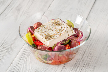 Fresh traditional Greek salad topped with thick feta slice served in glass bowl