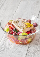 Fresh traditional Greek salad topped with thick feta slice served in glass bowl