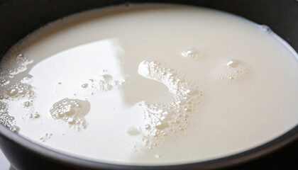 Boiling milk in a pan with bubbles and foam, close-up of hot creamy liquid, milk splashes on the walls, light steam, cooking process on the stove, home kitchen, culinary moment.