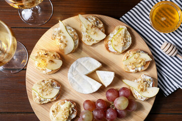 Delicious bruschettas served with camembert, grapes and wine on wooden table, flat lay
