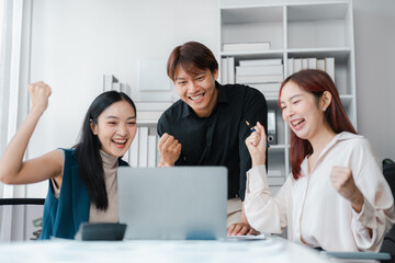 Fototapeta premium Asian Business Team Celebrating Success with Laptop in Modern Office Cheerful Adult Professionals Enjoying Win Teamwork and Positive Results