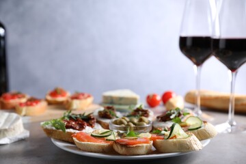 Different tasty bruschettas and red wine on grey textured table, closeup
