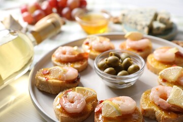 Tasty bruschettas with shrimps, lemon, sauce, olives and wine on white wooden table, closeup