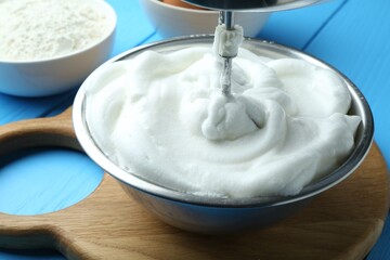 Whipped egg whites in bowl and mixer on blue wooden table, closeup