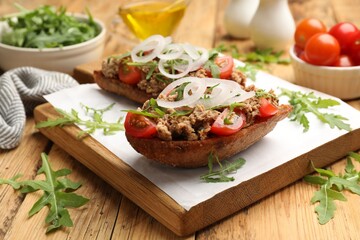 Delicious bruschettas with tuna, tomatoes, onion and arugula on wooden table, closeup