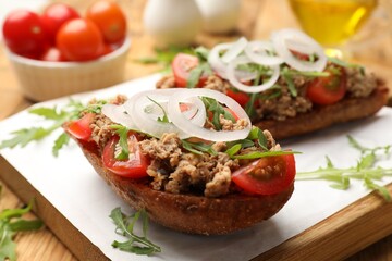 Delicious bruschettas with tuna, tomatoes, onion and arugula on wooden table, closeup