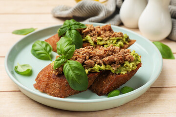 Delicious bruschettas with tuna, avocado and basil on light wooden table, closeup