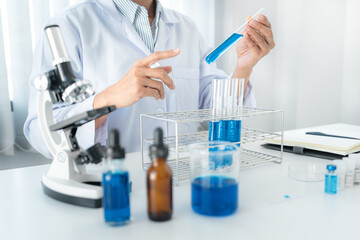 Fototapeta premium Scientist woman holding test tube to looking reaction on test tube with blue liquid in his hands while working