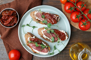 Delicious bruschettas with roast beef served on wooden table, flat lay
