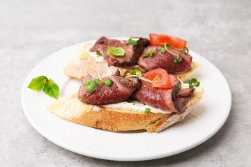 Delicious bruschettas with roast beef served on light table, closeup
