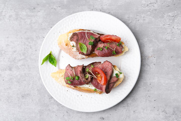 Delicious bruschettas with roast beef served on light table, top view