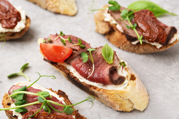 Delicious bruschettas with roast beef served on light table, closeup