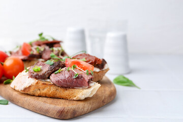 Delicious bruschettas with roast beef served on white tiled table, closeup. Space for text