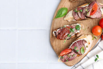 Delicious bruschettas with roast beef served on white tiled table, flat lay. Space for text