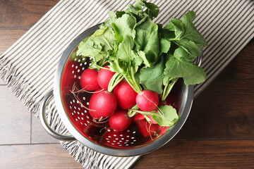 Fresh ripe radishes in colander on wooden table, top view