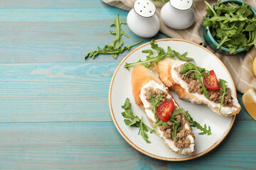 Delicious bruschettas with tuna, cream cheese and tomatoes on light blue wooden table, flat lay....