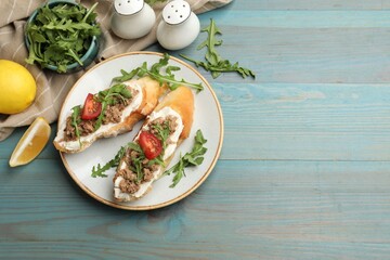 Delicious bruschettas with tuna, cream cheese and tomatoes on light blue wooden table, flat lay....