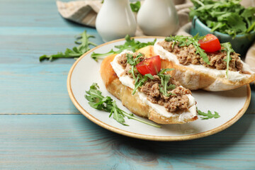 Delicious bruschettas with tuna, cream cheese and tomatoes on light blue wooden table, closeup