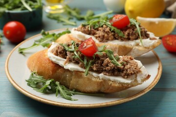 Delicious bruschettas with tuna, cream cheese and tomatoes on light blue wooden table, closeup