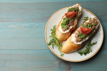 Delicious bruschettas with tuna, cream cheese and tomatoes on light blue wooden table, top view. Space for text