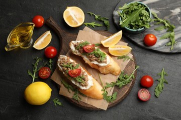 Delicious bruschettas with tuna, tomatoes, arugula, lemons and oil on grey table, flat lay