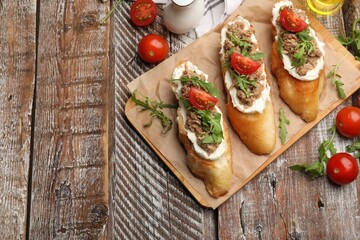Delicious bruschettas with tuna, tomatoes and arugula on wooden table, flat lay. Space for text