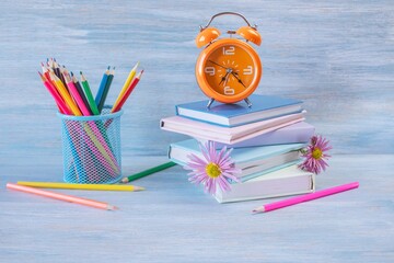 Back to school. Books and colorful pencils, an alarm clock and flower bookmarks on a wooden table....