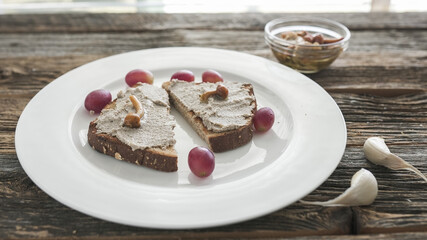 Delicious spread on bread served with fresh grapes and mushrooms on a rustic wooden table