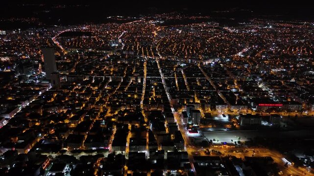 Vast urban landscape of mersin at night glowing with golden streetlights, showing the grid like pattern of roads and building rooftops from a stunning high angle aerial perspective