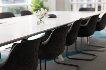 Large white meeting table and grey empty chairs in office