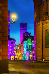 Christmas illumination on a medieval tower and cobbled square in Alba, Italy, at dusk