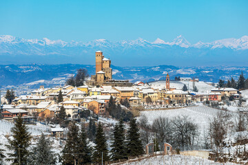 A picturesque winter scene of a village with snow-covered rooftops among rolling hills and vineyards in Italy.