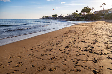 A deserted beach at sunset with wet sand textures, calm waves, and the silhouetted old town peninsula under warm pre-sunset light. Serene spring evening in Side, Antalya, Turkey.

