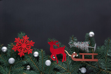 Christmas festive fairy frame and greeting card. A toy of red deer drive by sledge a Christmas tree on black background with copy space. Top view.